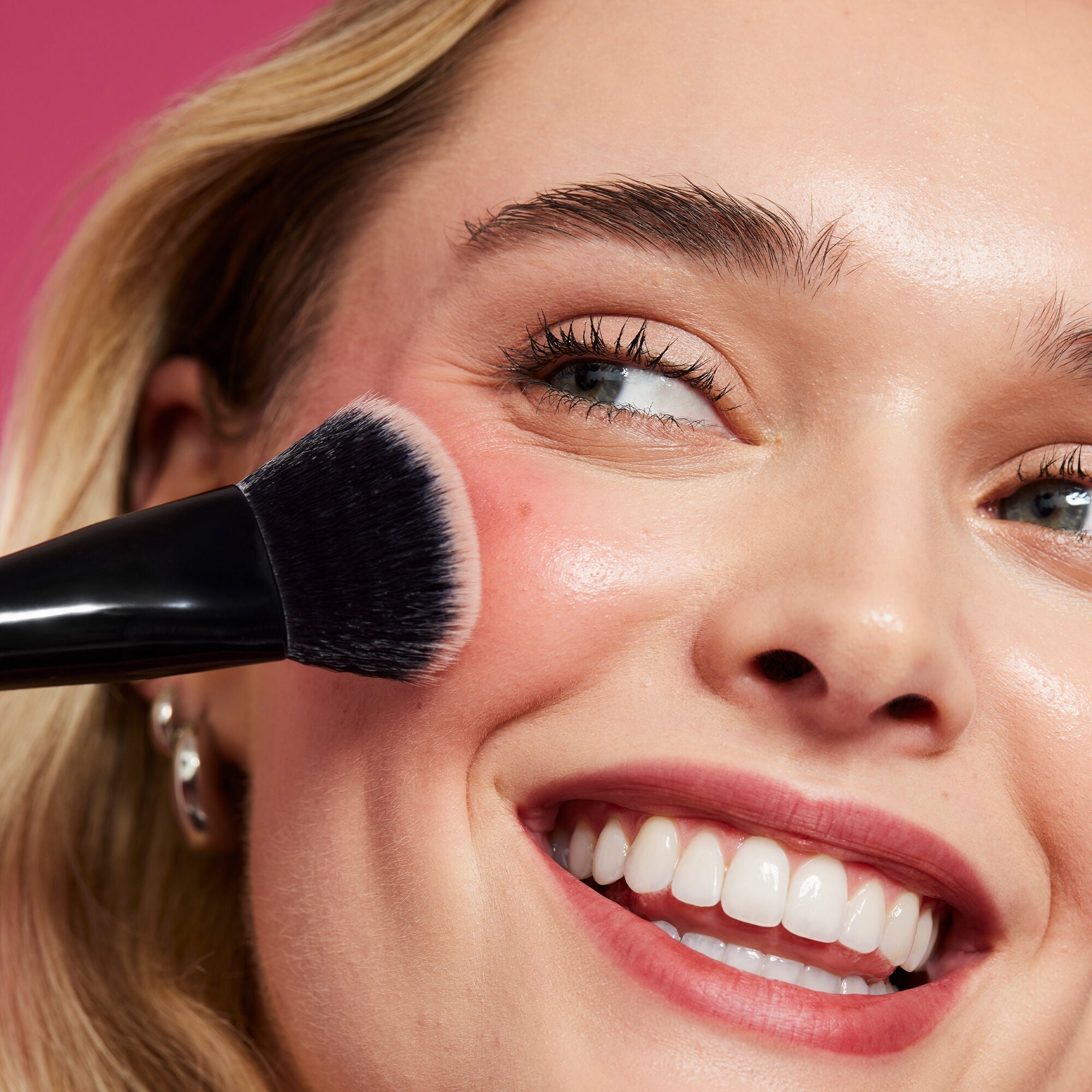 Modelo aplicando rubor rosado en la mejilla con una brocha de maquillaje.