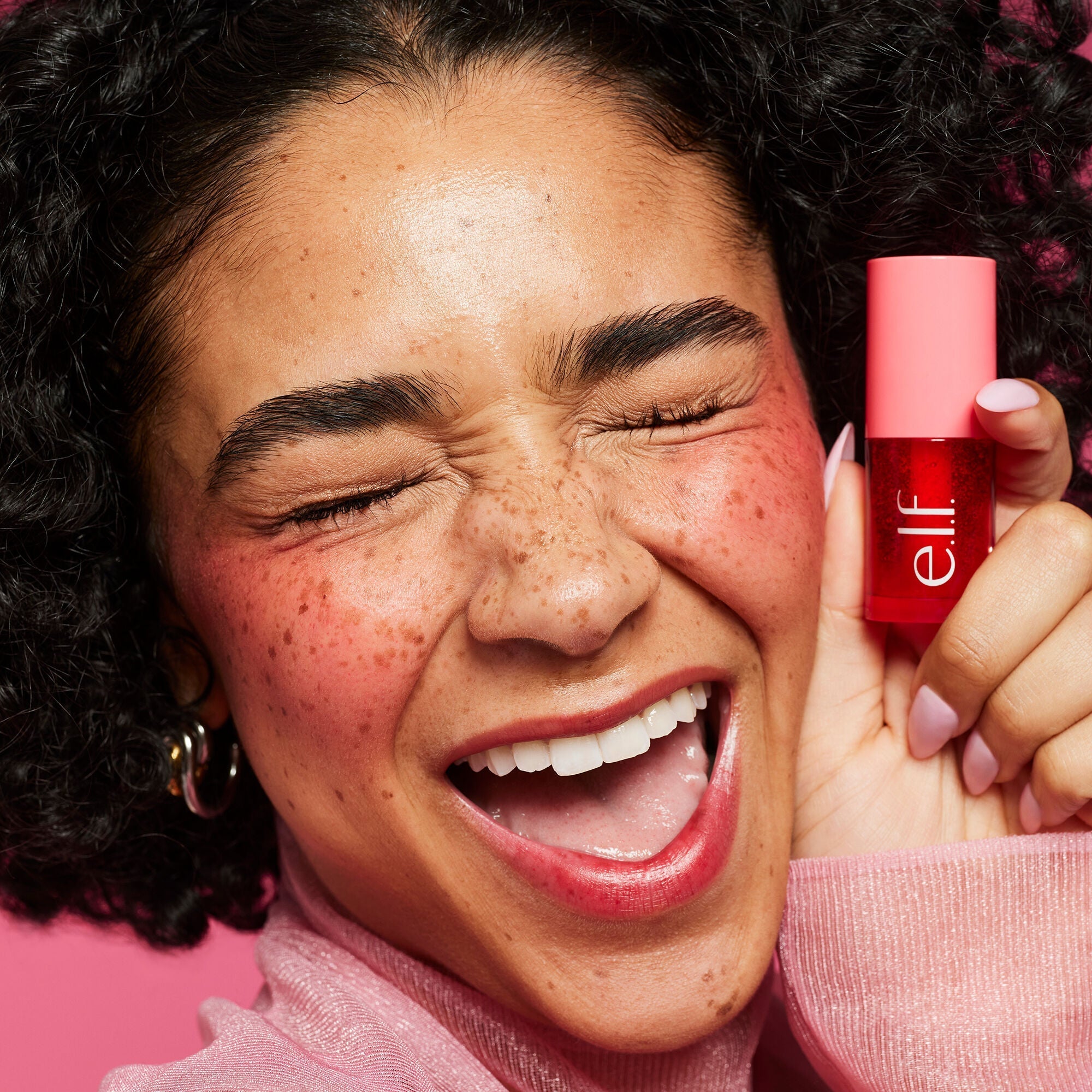 Modelo sosteniendo un envase rojo de e.l.f. Sheer For It Blush Tint junto al rostro.